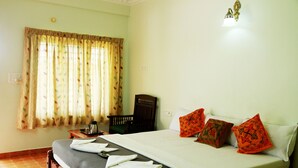 A neatly made bed with a grey bedspread, two orange pillows, and a wooden headboard. - Cosy Regency (Ambalapuzha)