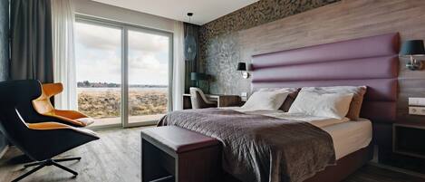 A modern hotel room with a large bed, a desk, a chair, and a view of the outdoors.