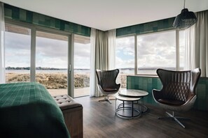 A room with a bed, two leather chairs, a small round table, and a view of a natural landscape through large windows. - Hotel Kriunes - A city hotel by the lake (Kópavogur)