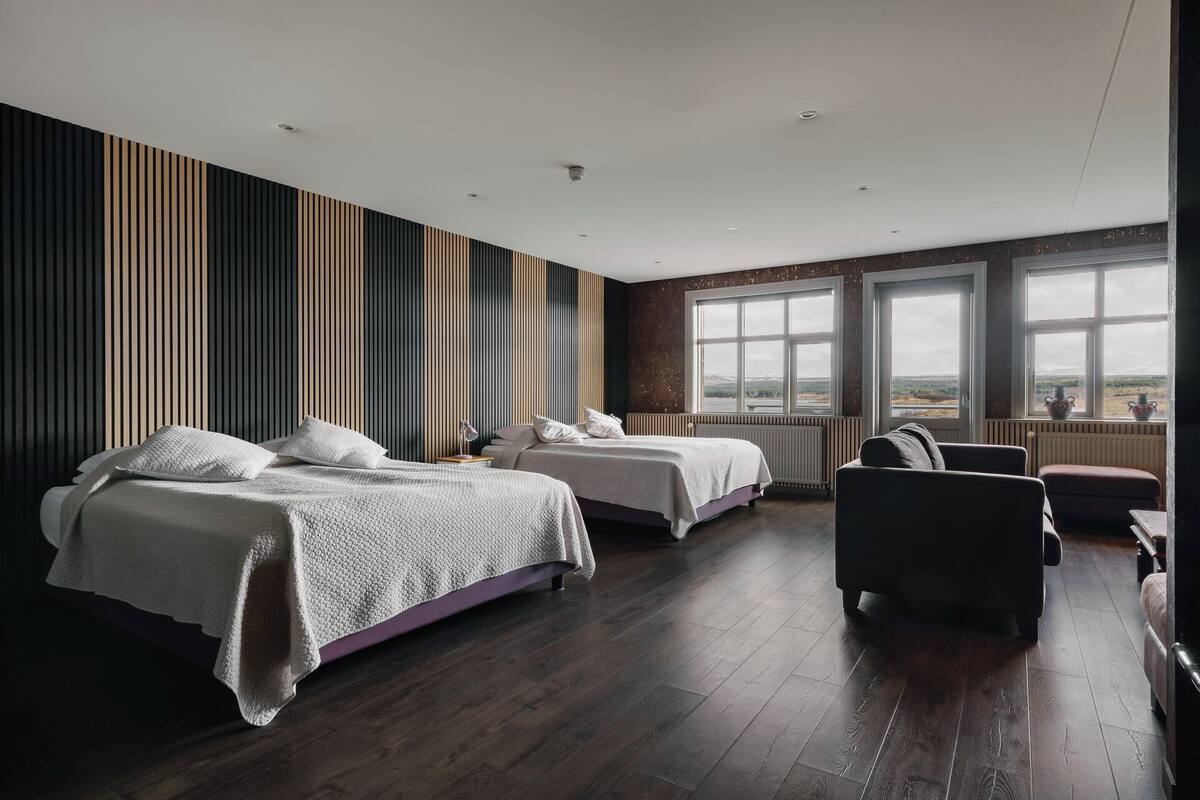 Et moderne hotelværelse med to senge, en sofa og store vinduer med udsigt.
