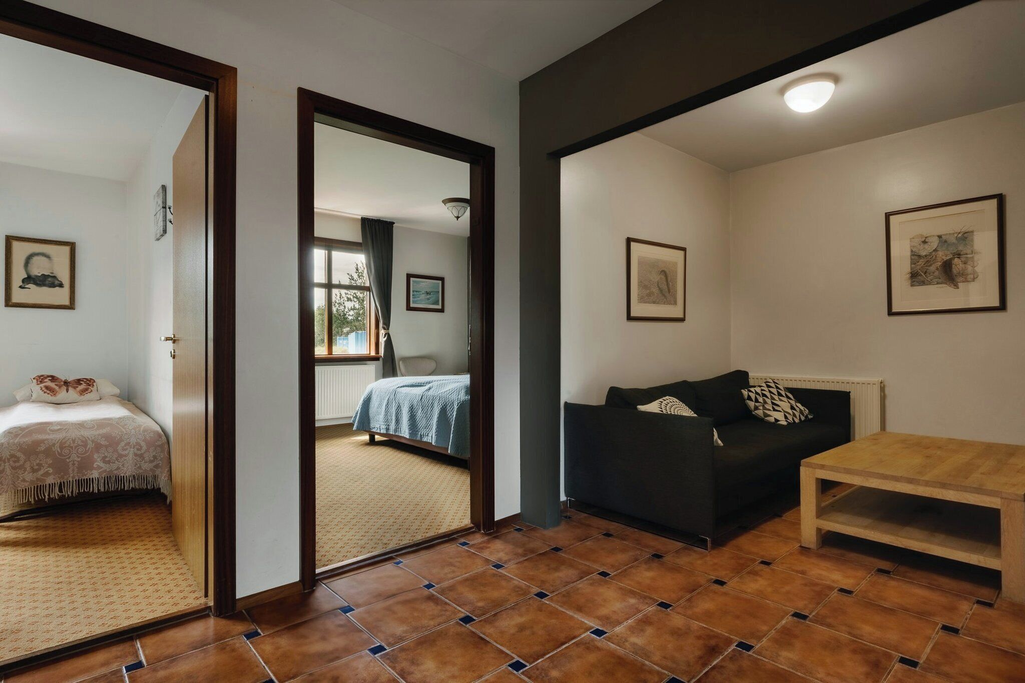 Una habitación con una cama, un sofá negro, una mesa de madera y vistas a través de un umbral abierto.