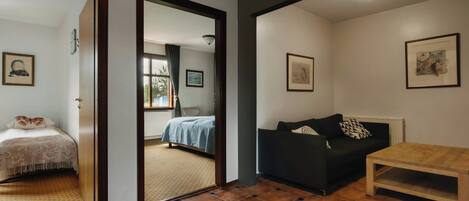 Una habitación con una cama, un sofá negro, una mesa de madera y vistas a través de un umbral abierto.