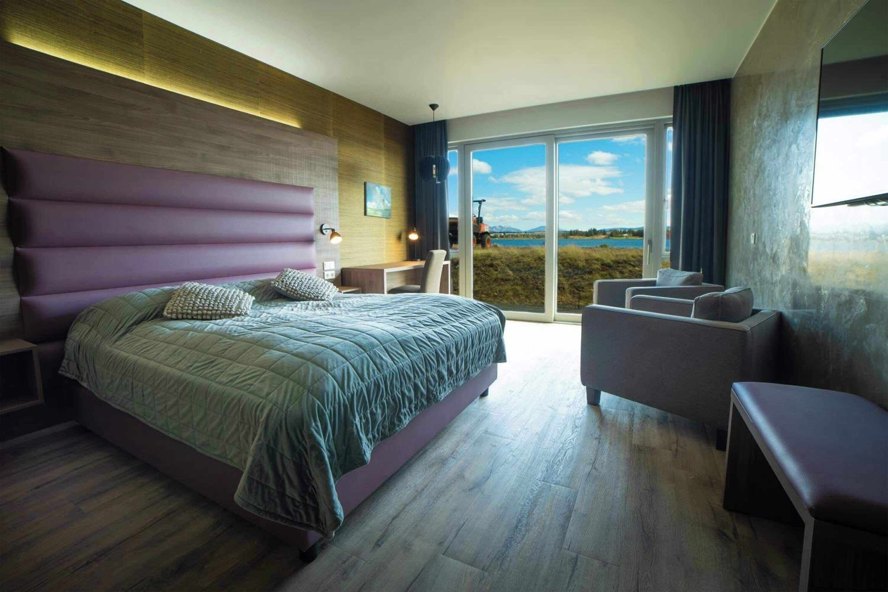 A modern bedroom with a large bed, a desk, and a view of a lake.