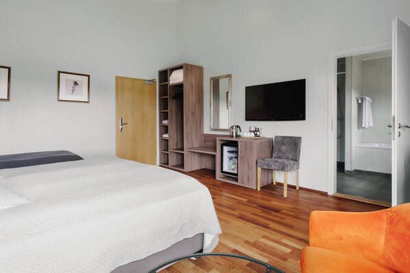 A bedroom with a bed, a wardrobe, a desk with a chair, a television, and a bathroom visible through an open door.