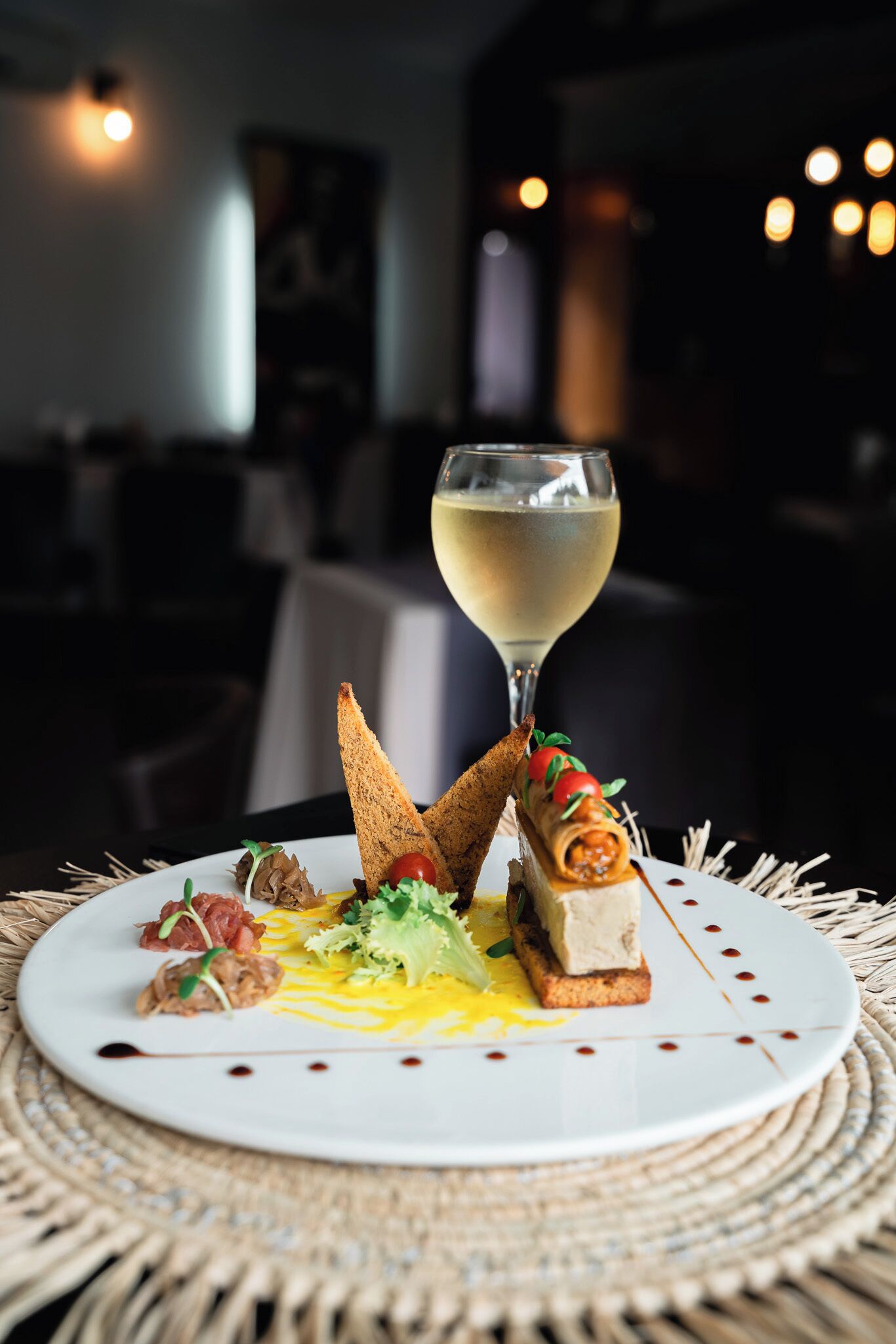 Ein Teller Essen mit einem Glas Weißwein auf einer gewobenen Tischmatte.