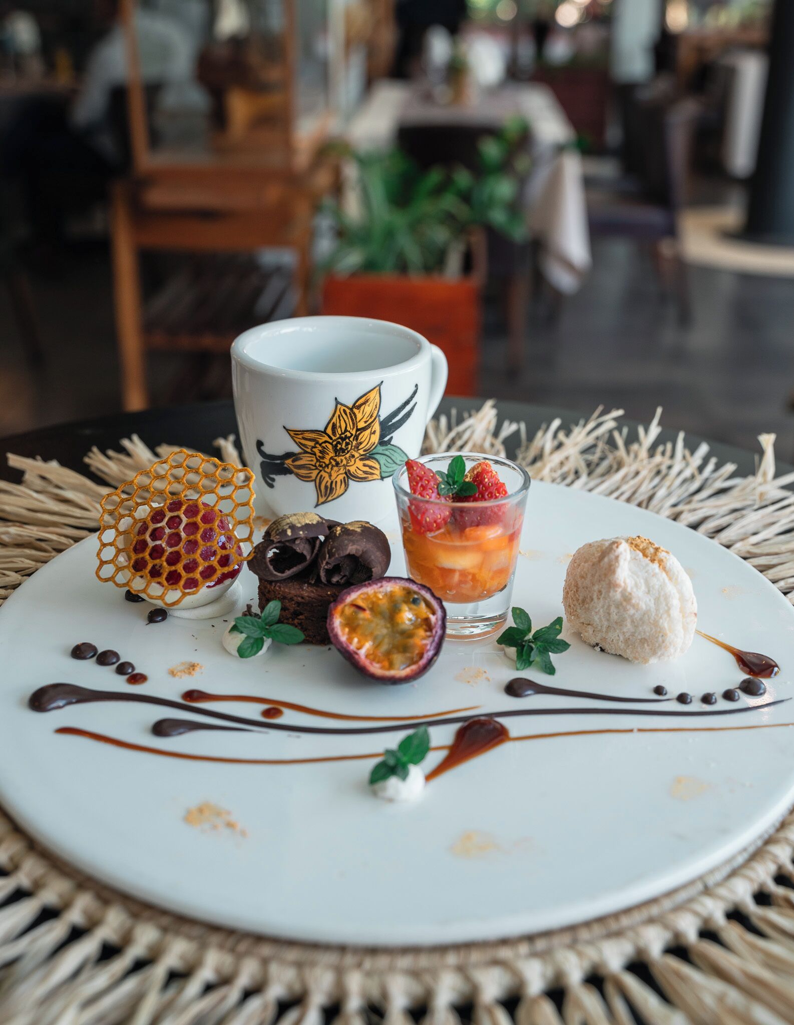 A dessert plate with a coffee mug, a glass of drink, and a pastry on a woven table mat.