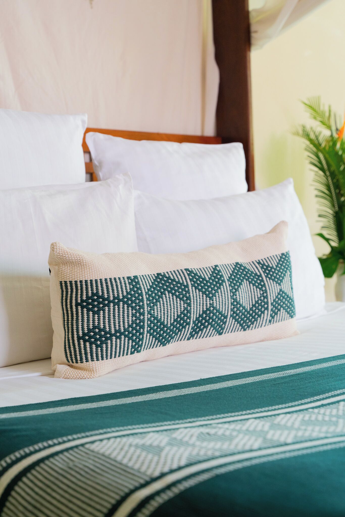 A bed with white and green patterned pillows, a green and white striped bedspread, and a wooden headboard.