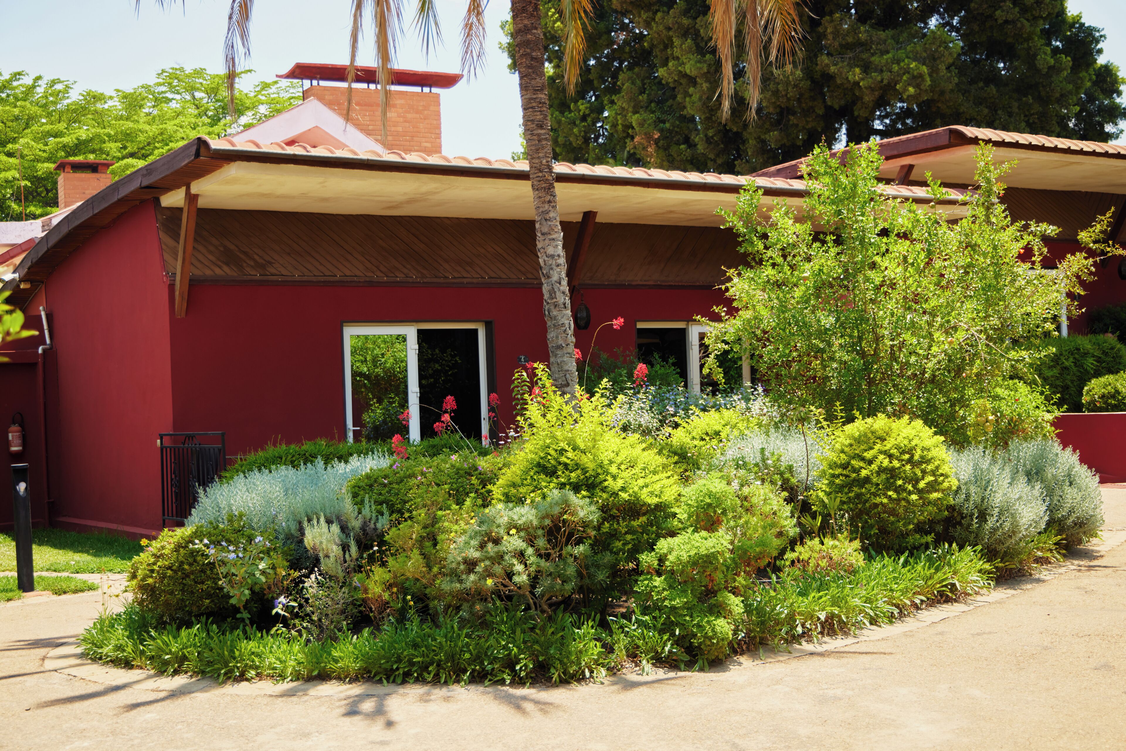 Un bâtiment rouge doté d’un porche abrité, entouré d’une végétation luxuriante et d’un jardin bien entretenu.