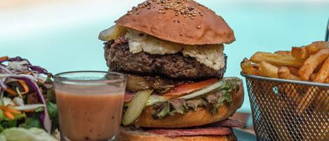 Hamburguesa con un cuchillo encima, un vaso de salsa, papas fritas y una ensalada sobre una tabla de madera.