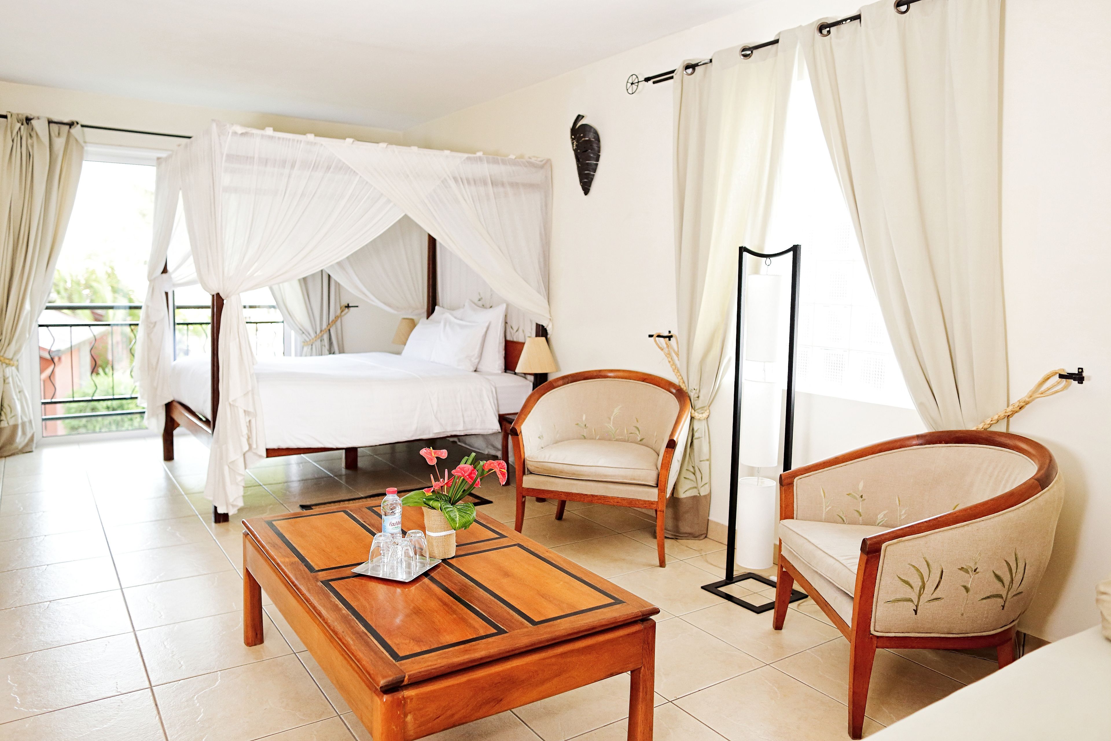 A hotel room with a bed, two chairs, a coffee table, and a large window with curtains.