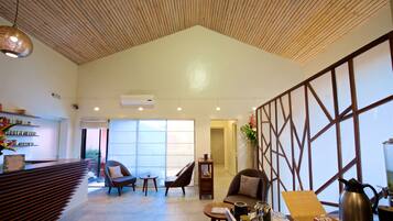 A spacious lobby with a wooden ceiling, a reception desk, seating area, and a large window providing natural light.