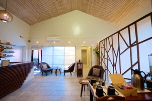 A spacious lobby with a wooden ceiling, a reception desk, seating area, and a large window providing natural light.
