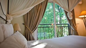 A bedroom with a bed, curtains, a window with a view of trees, and a lamp.