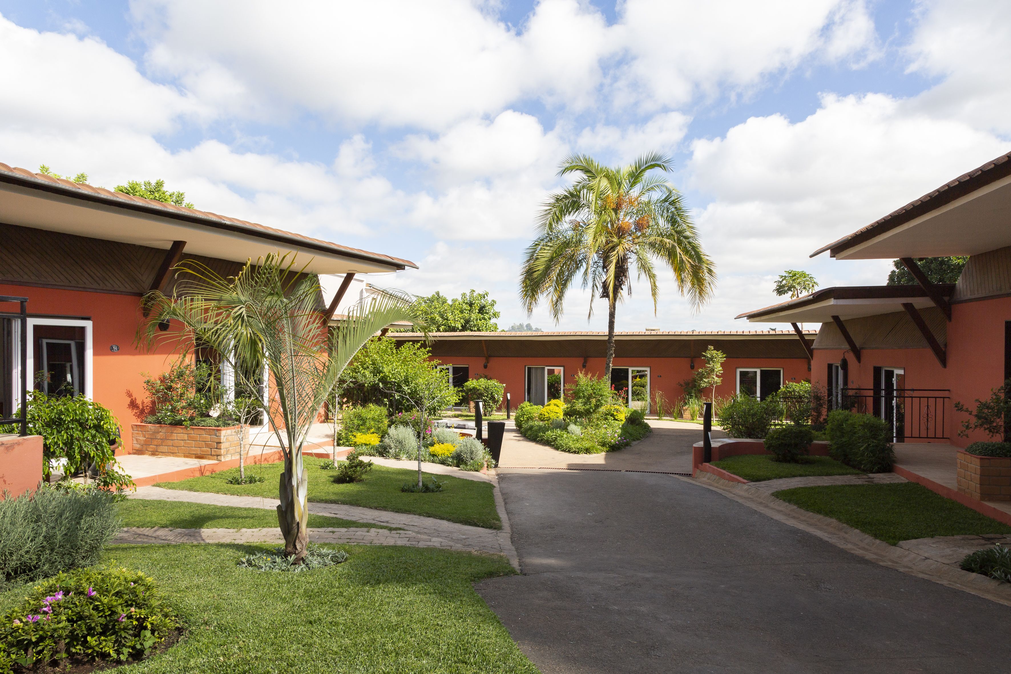 A residential area with two-story houses, a paved driveway, and well-maintained gardens with palm trees and shrubs.