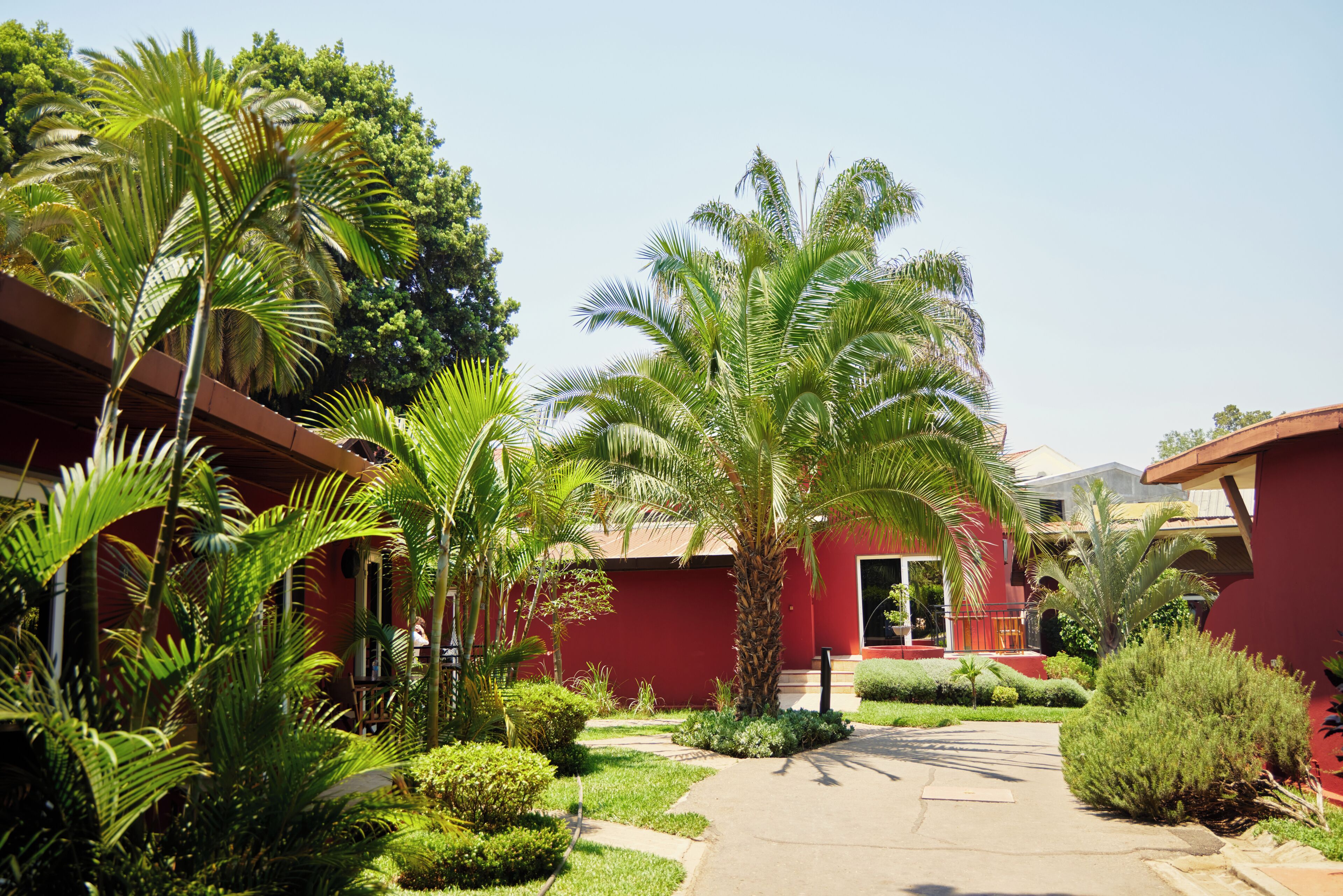 A red building with a central courtyard surrounded by palm trees and greenery.