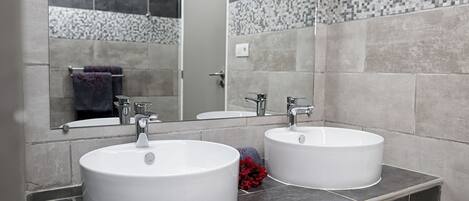 Une salle de bain avec deux lavabos blancs, un miroir et un mur recouvert de carreaux.