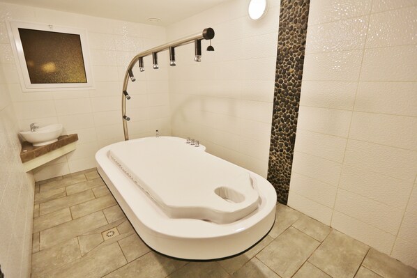 A bathroom with a white bathtub, a sink, and a showerhead. - Relais des Plateaux (Antananarivo)