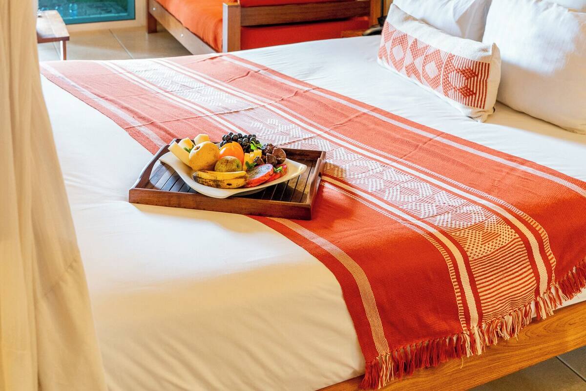 A bedroom with a canopy bed, a tray of fruit, and a view of the outdoors.