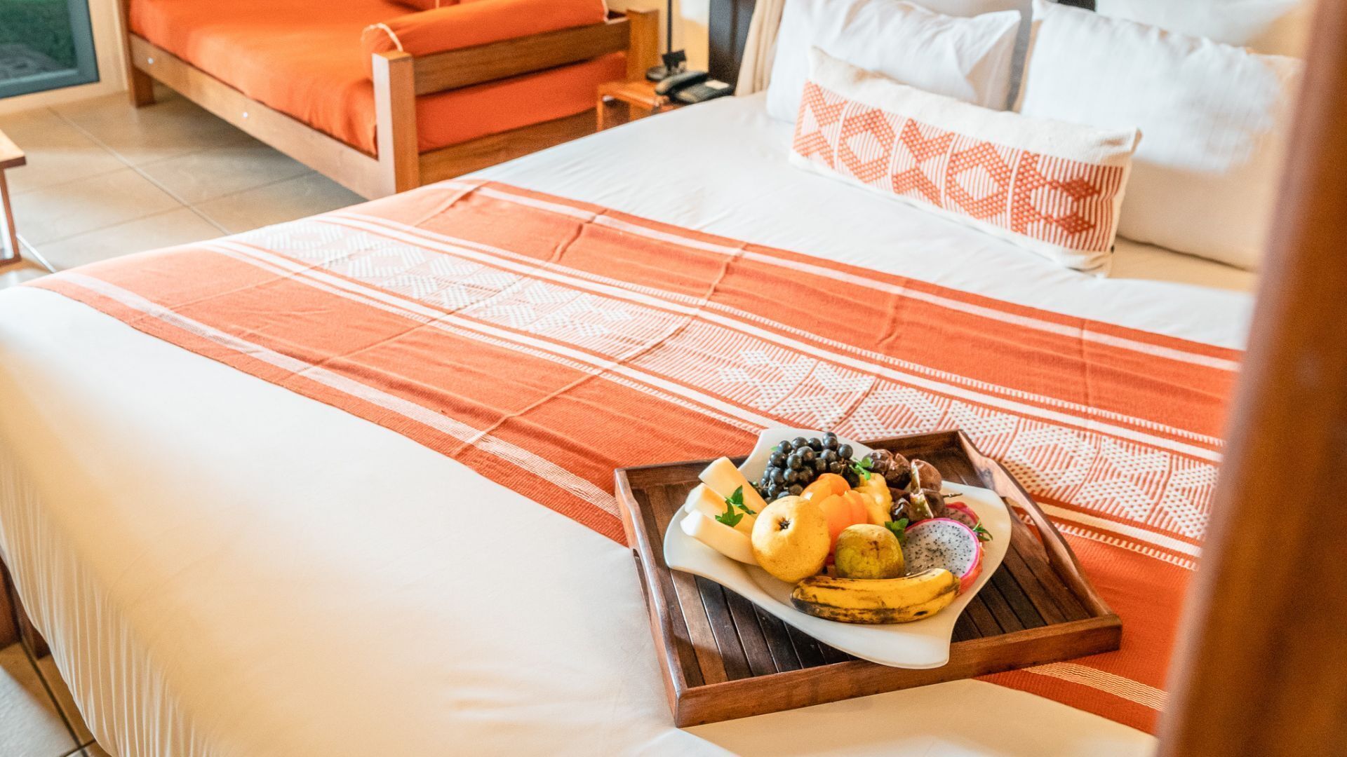 Une chambre d’hôtel avec un lit, une table de chevet en bois et un plateau avec des fruits et du fromage.