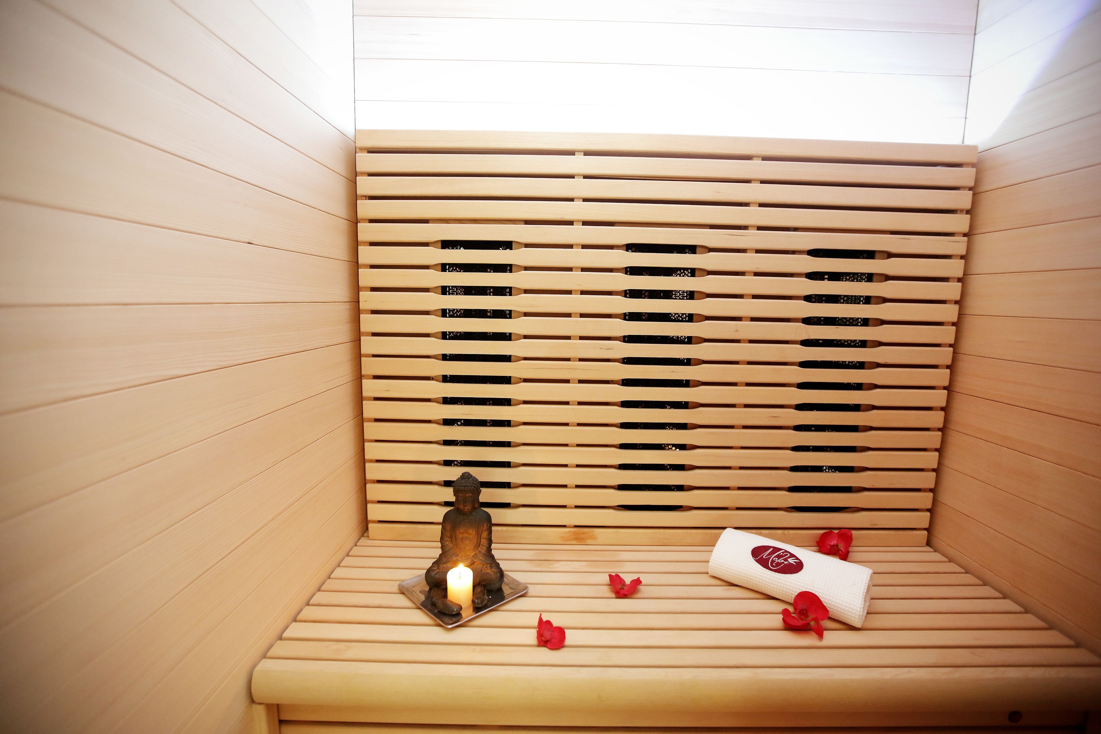 A wooden sauna with a small Buddha statue, a lit candle, and a rolled towel.