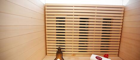 A wooden sauna with a small Buddha statue, a lit candle, and a rolled towel.