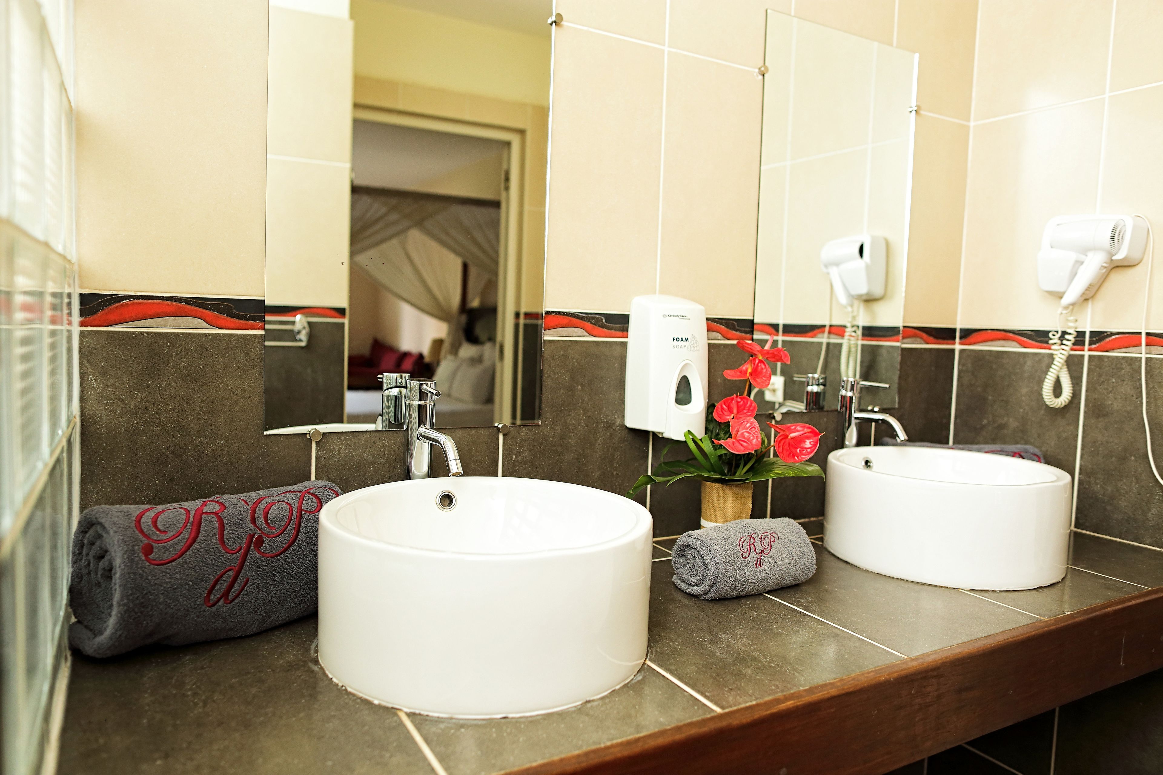 A bathroom with two sinks, a towel rack with towels, a hand dryer, and a soap dispenser.