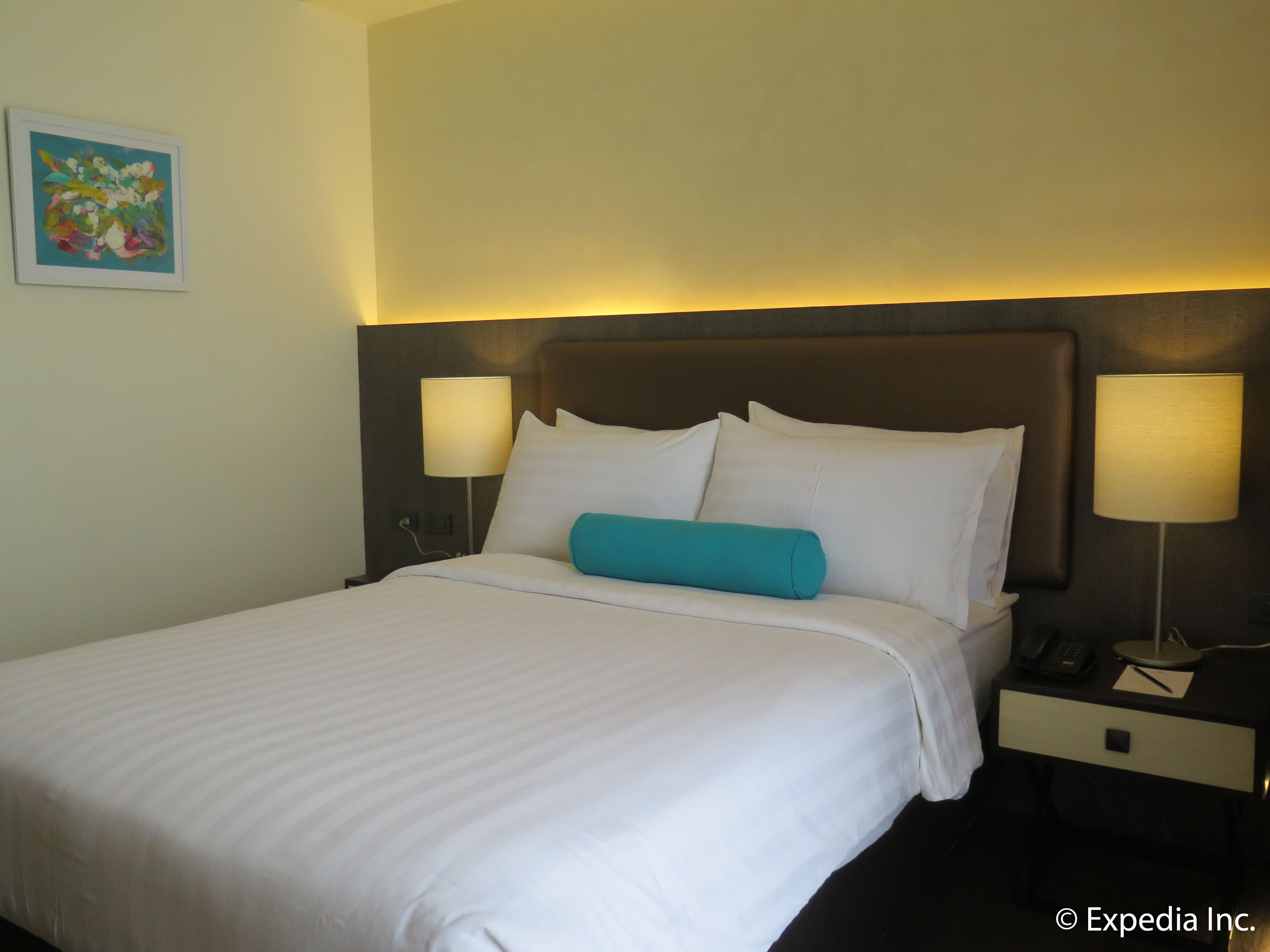 A neatly made bed with white linens, a teal accent pillow, and two bedside lamps.