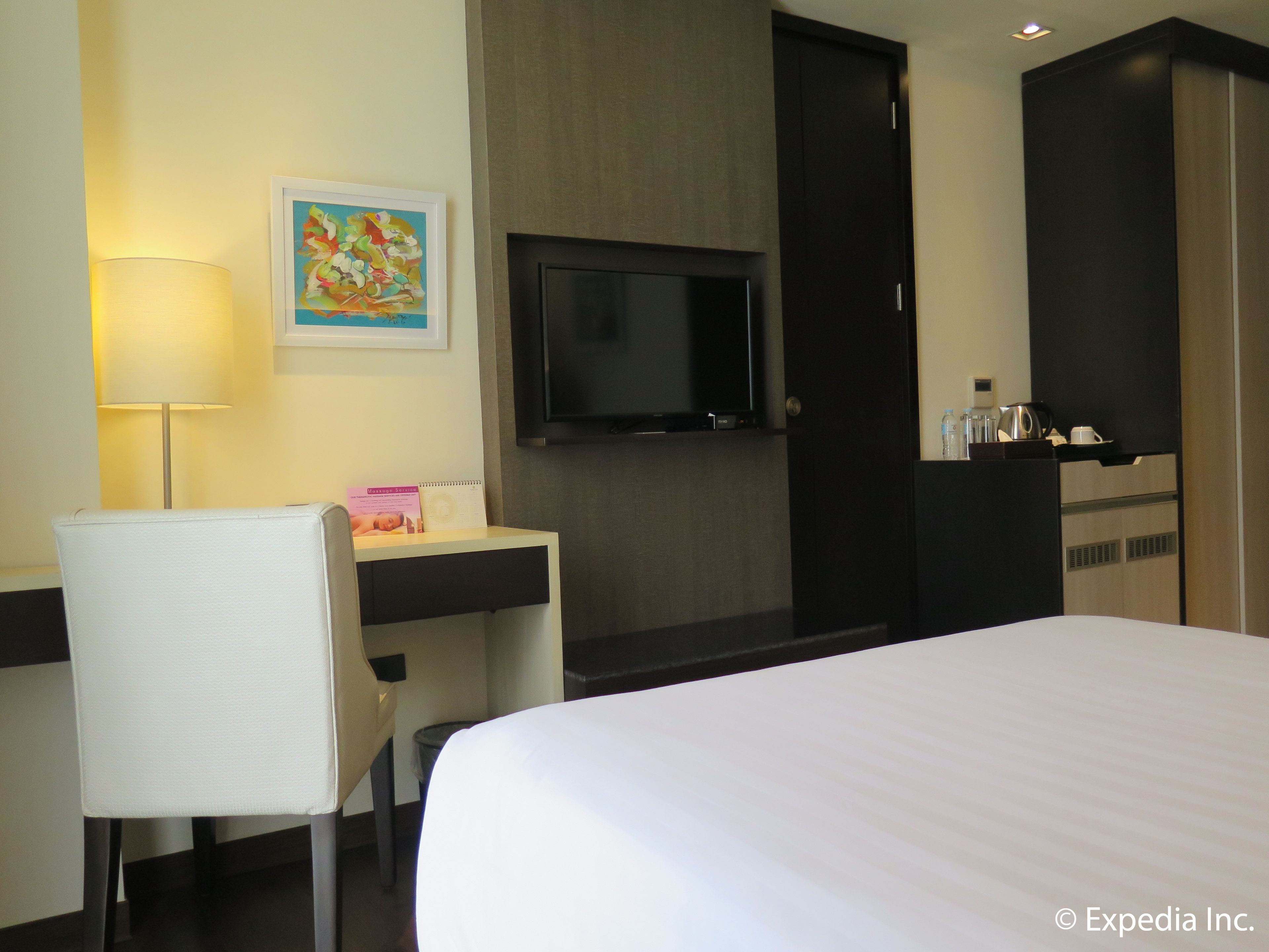 Une chambre d’hôtel comprenant un lit, un bureau avec une chaise, une télévision, un tableau au mur et un mini-bar.