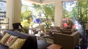 Un salón moderno con un sofá, sillones y una mesa de centro. Amplios ventanales ofrecen vistas a la calle y al verdor exterior.