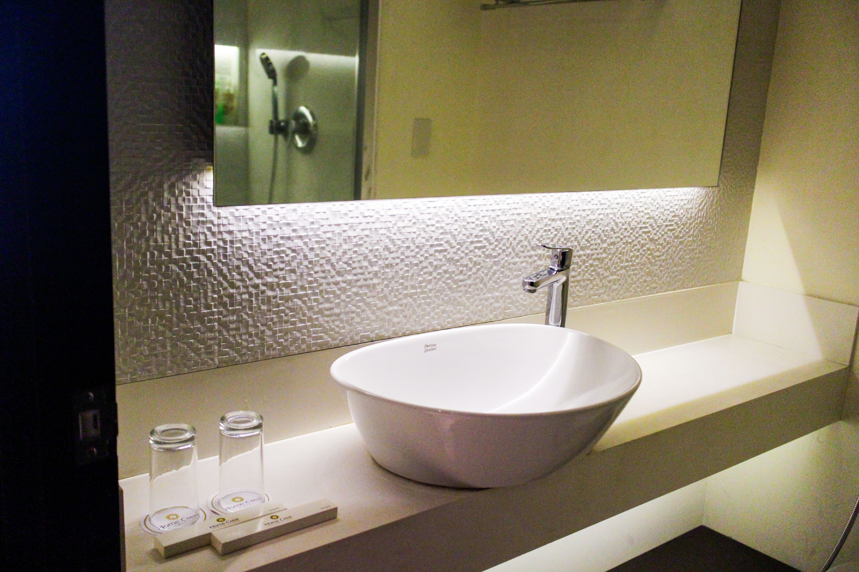 A bathroom with a white vessel sink, a mirror above it, and a textured wall.