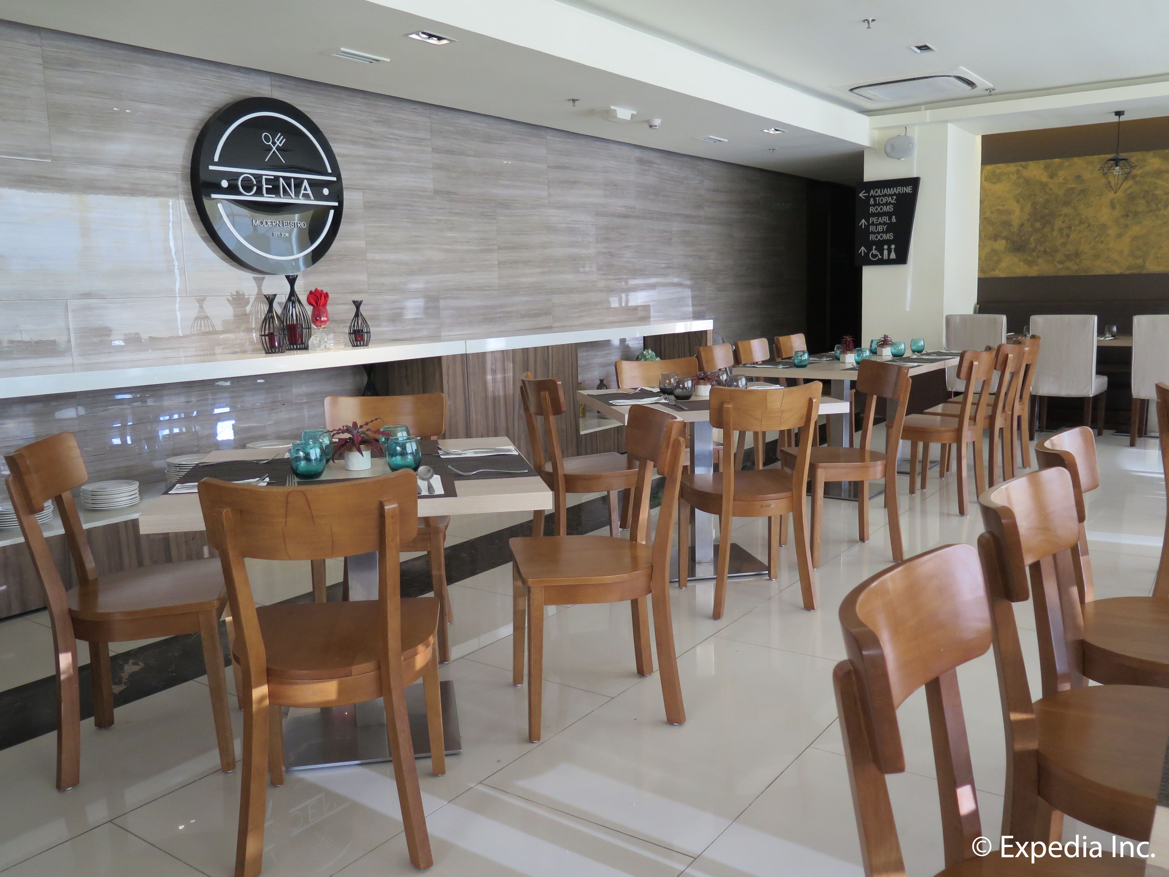 A modern dining area with wooden chairs and tables, a wall-mounted sign reading "OENA MODERN BISTRO", and directional signs for "Aquamarine Topaz Rooms" and "Ruby Rooms".