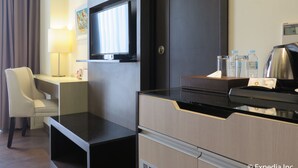 Habitación de hotel con escritorio, silla, televisor, minibar y cafetera.