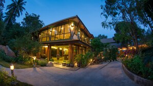 A two-story building with large windows and a covered entrance area, surrounded by lush greenery and palm trees. - Tanote Villa (Koh Tao)