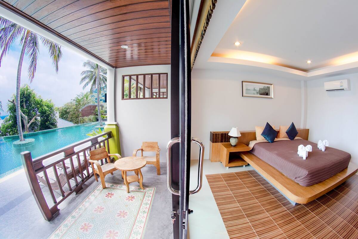 A hotel room with a balcony, a bed, a desk, and a view of the pool.