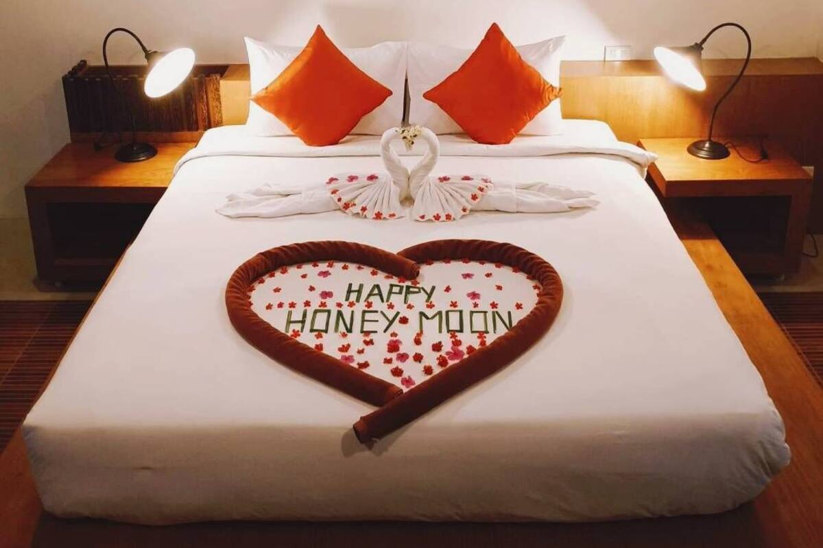 A hotel room with a neatly made bed, two nightstands with lamps, a framed picture on the wall, and a heart-shaped decoration on the bed.