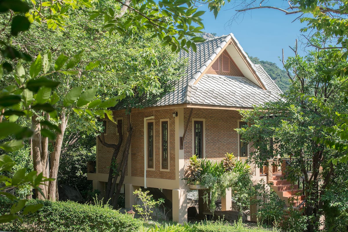 A brick house with a sloped roof, surrounded by lush greenery and trees.