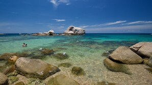 A clear blue sea with large rocks in the foreground and a person swimming in the water. - Tanote Villa (Koh Tao)