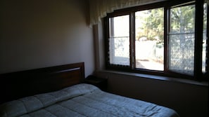 A bedroom with a single bed, a nightstand, and a window with a view of trees. - Rifugio del Pettirosso (Pescasseroli)