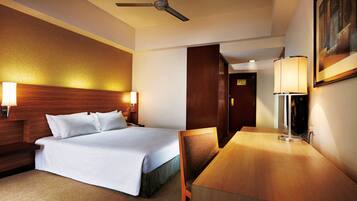 A hotel room with a bed, a desk, a chair, a ceiling fan, and two wall-mounted lamps.