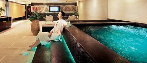 A person relaxing by a poolside in a modern indoor setting with a television and plants visible in the background.