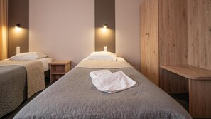 A hotel room with two beds, a wooden wardrobe, and a nightstand.