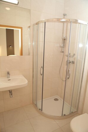 Un baño con ducha de vidrio, lavamanos e inodoro.
