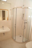 Un baño con ducha de vidrio, lavamanos e inodoro.