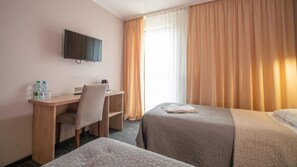 A hotel room with a desk, two beds, a television, and a window with curtains.
