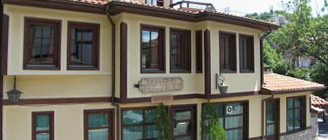 Un edificio de dos pisos con múltiples ventanas, un letrero que dice 'Hotel' y escalones de piedra que conducen a la entrada.