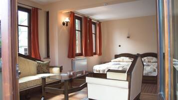 A hotel room with a sofa, a glass-top table, a bed with a headboard, and a window with curtains.