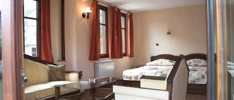 A hotel room with a sofa, a glass-top table, a bed with a headboard, and a window with curtains.