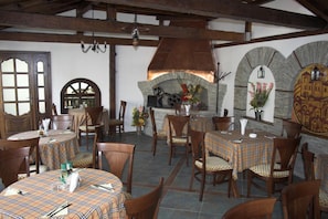 A restaurant interior with round tables, wooden chairs, a stone fireplace, and a vaulted ceiling. - Hotel Old Times (Asenovgrad)