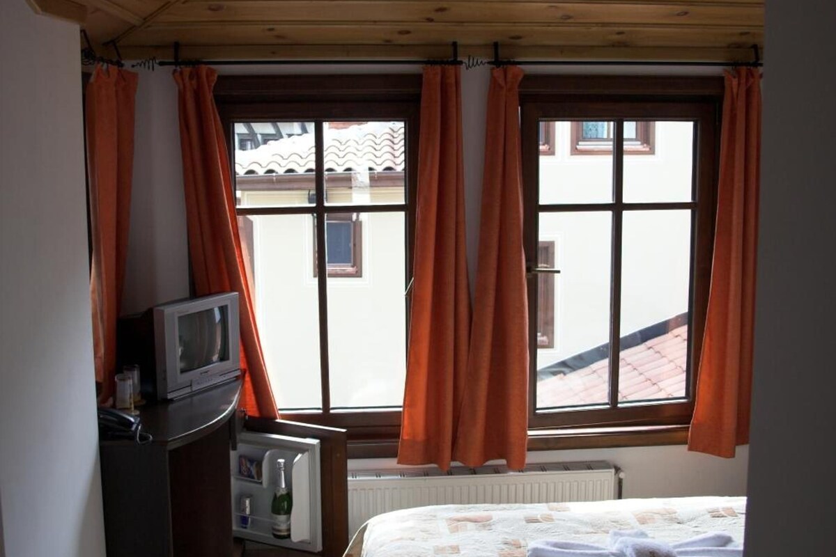 A bedroom with a bed, a television, a radiator, and a window with curtains.