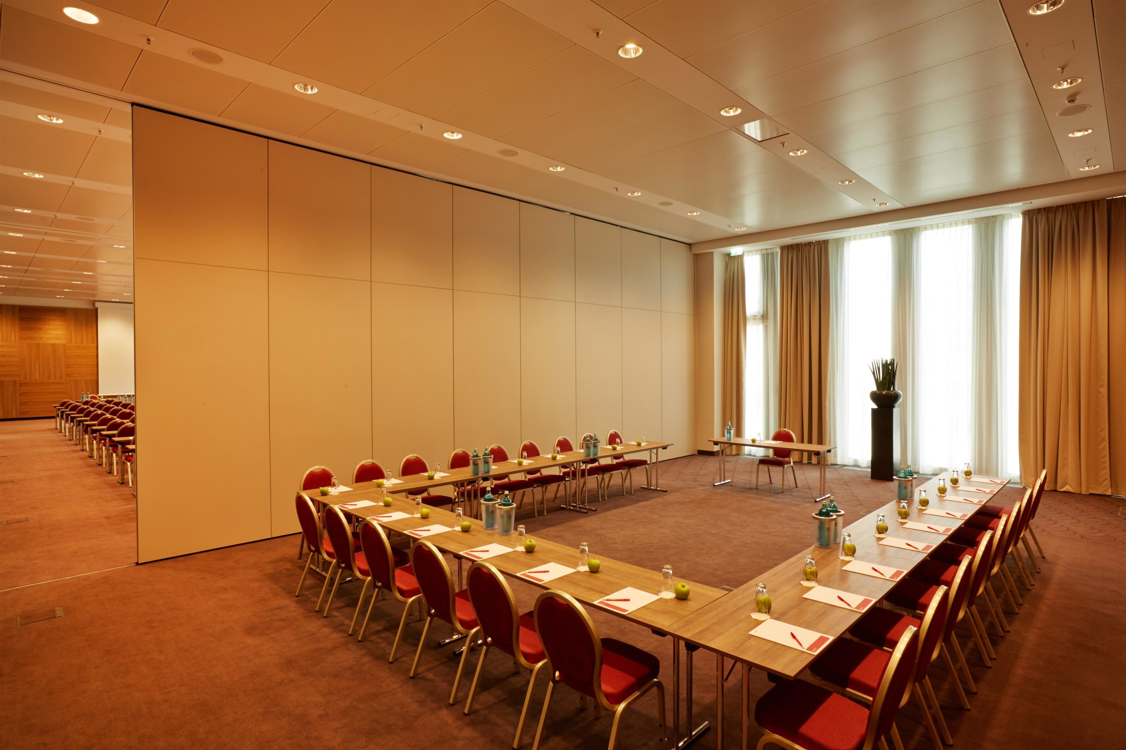 A conference room with a long table, red chairs, and a large window with curtains.